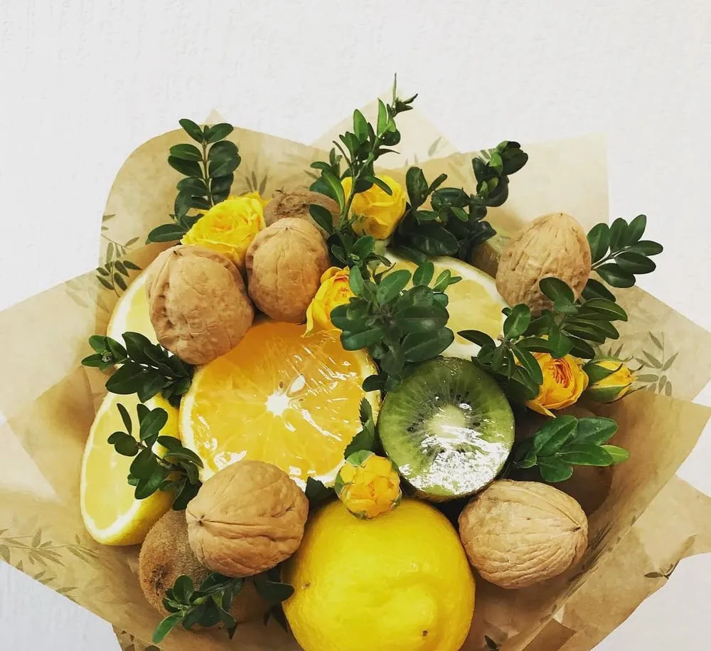 Augļu pušķis ar citroniem, kivi un valriekstiem zaļā lapu ietvarā