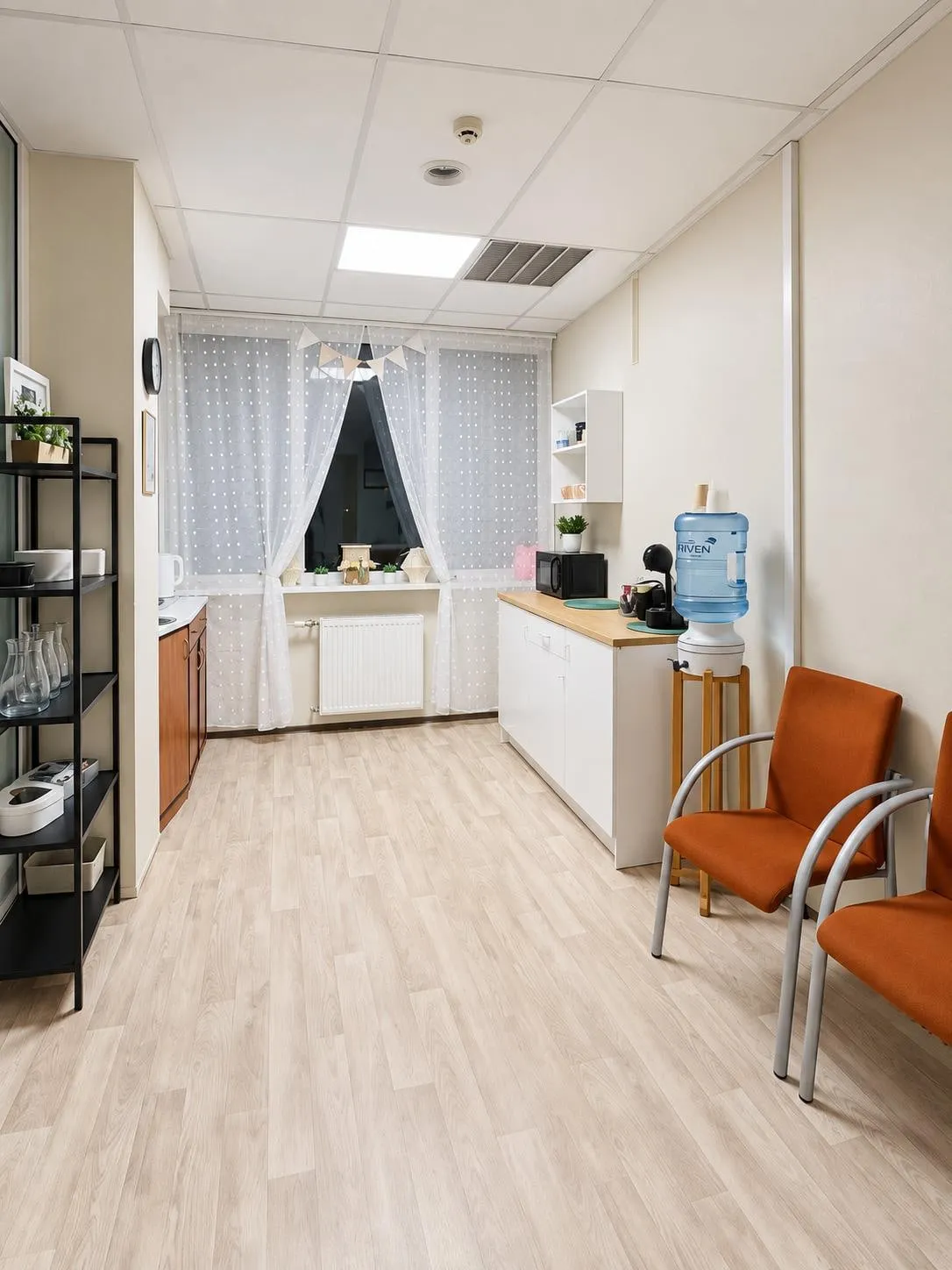 Virtuve ar darba virsmu, kafijas automātu, ūdens dzesētāju, traukiem plauktos un krēsliem
